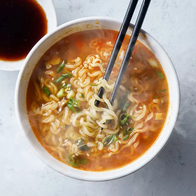 A bowl of chicken noodles with 2 chop sticks