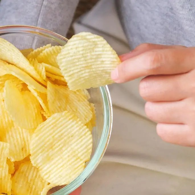 Someone taking one crisp out of a glass bowl with crisps