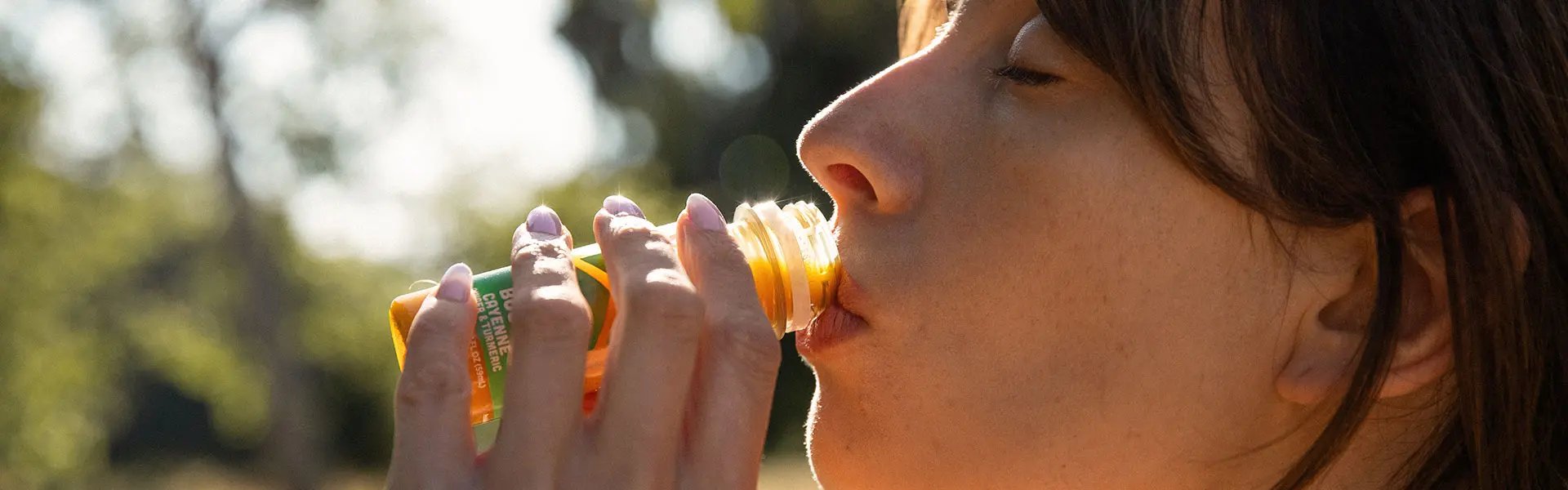 Young woman with closed eyes, close up, drinking fruit juice from a very small bottle